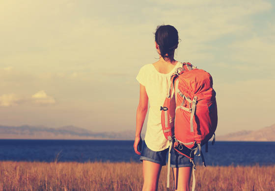 Young female backpacker with her back to the camera looking forward to a fairly flat landscape, some hills and mountains in the distance