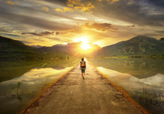 Man walking away from the camera into a sunset and towards mountain range