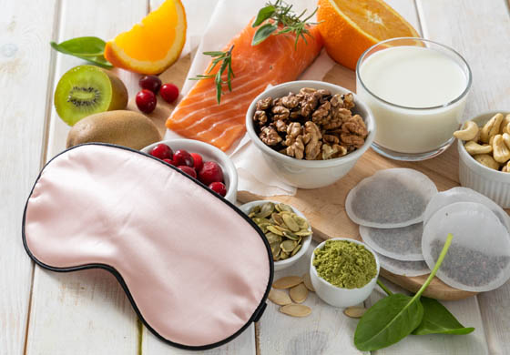 Sleep mask on top of healthy, nutritious snacks and food that enhances sleep (including salmon, nuts, and more)