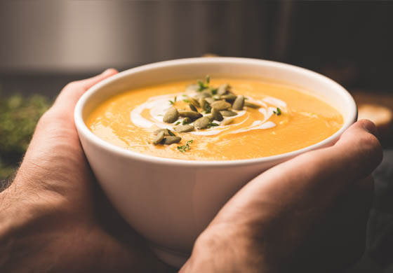 Close-up of man holding a big bowl of soup (pumpkin soup with pumpkin seeds on top) with both hands