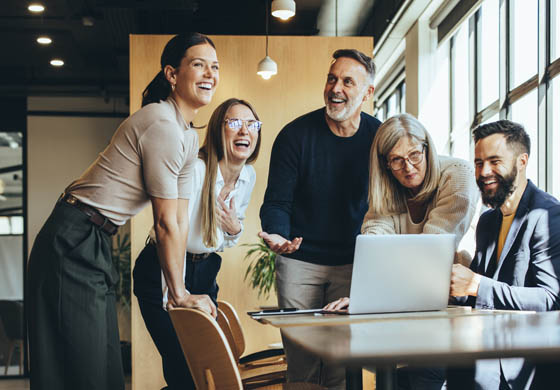 Happy workplace with colleagues leaning over a table and laptop working together